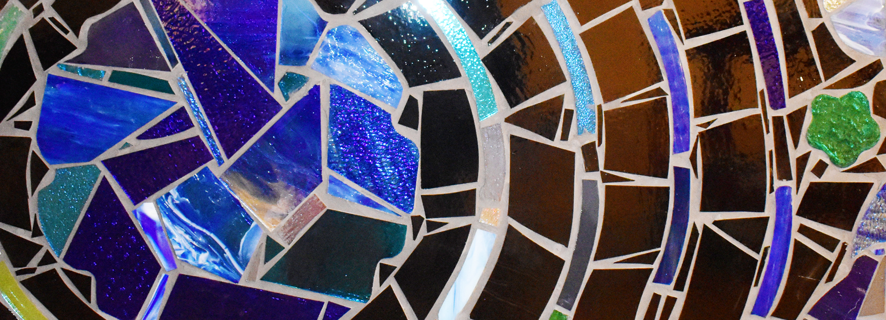 A close-up shot of a stained-glass mosaic with green, blue, and clear tiles.